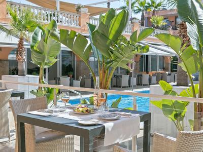 Table with food next to pool in tropical hotel garden with seating area and plants.