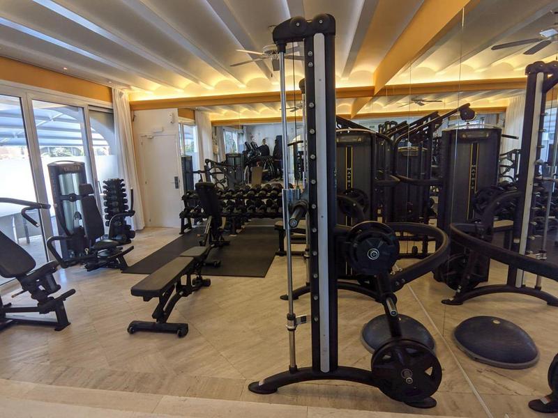 Brightly lit gym with various workout machines and mirrors on the walls.