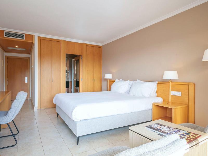 Modern hotel room with large bed, desk, chairs, and warm wood accents.