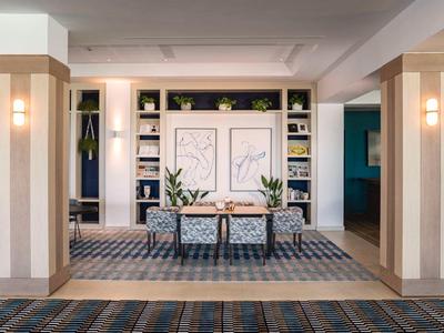 Hall d'hôtel moderne avec coin salon, plantes et panneaux muraux décoratifs.