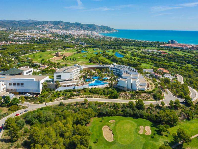 Vue aérienne d'un complexe avec piscine, terrain de golf et vue sur la mer dans un cadre verdoyant.