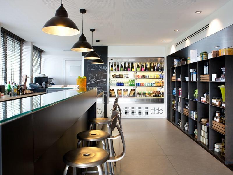 Espace bar d'hôtel moderne avec tabourets, étagères et station de boissons éclairée.