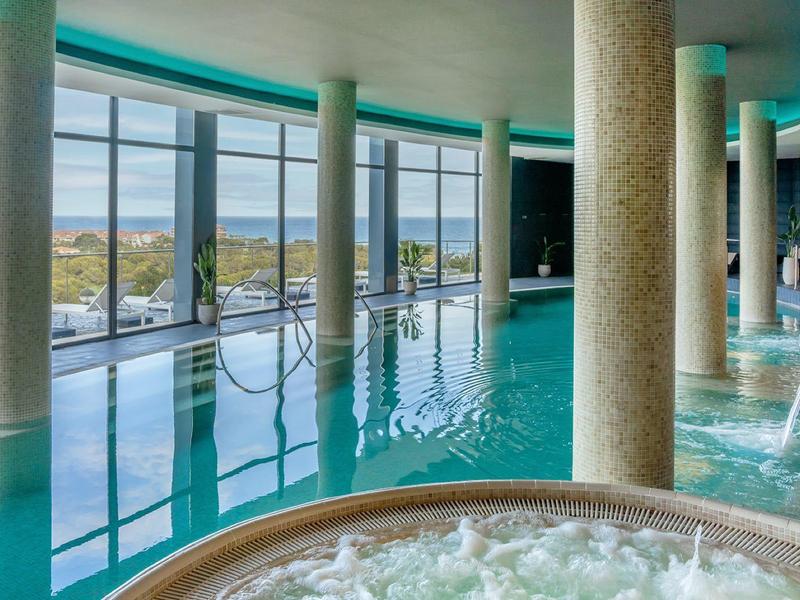 Piscine intérieure moderne avec grandes fenêtres, piscine et jacuzzi avec vue sur le paysage.