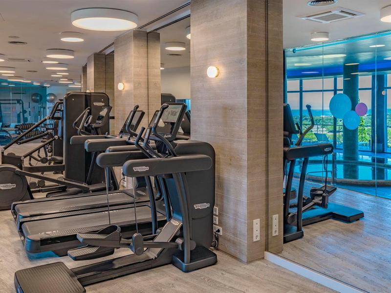 Équipements de fitness modernes dans une salle de sport d'hôtel lumineuse avec fenêtres en verre.