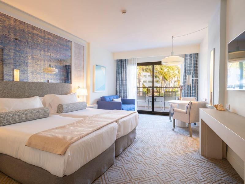 Chambre d'hôtel lumineuse avec deux lits simples, balcon et décoration moderne.