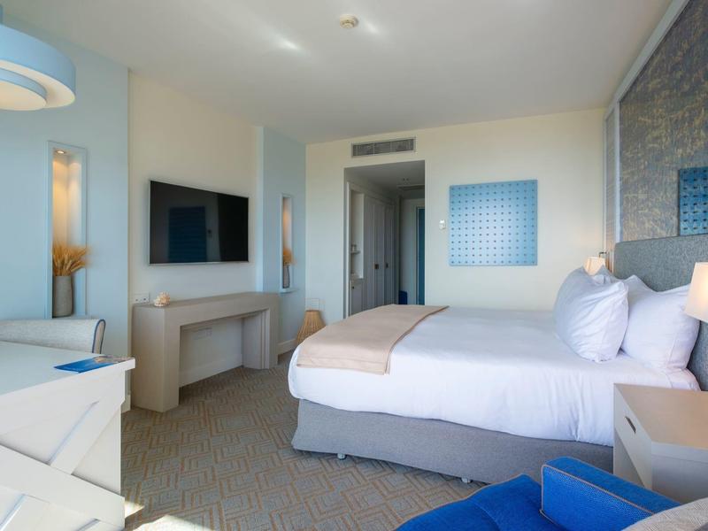 Chambre d'hôtel lumineuse avec grand lit, canapé et décoration moderne.