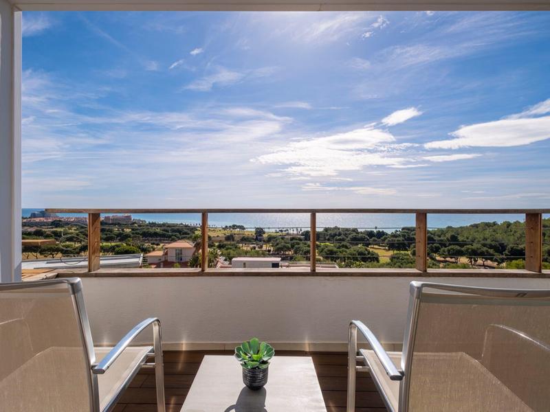 Balcon avec deux chaises et une petite table avec vue sur la mer sous un ciel nuageux.