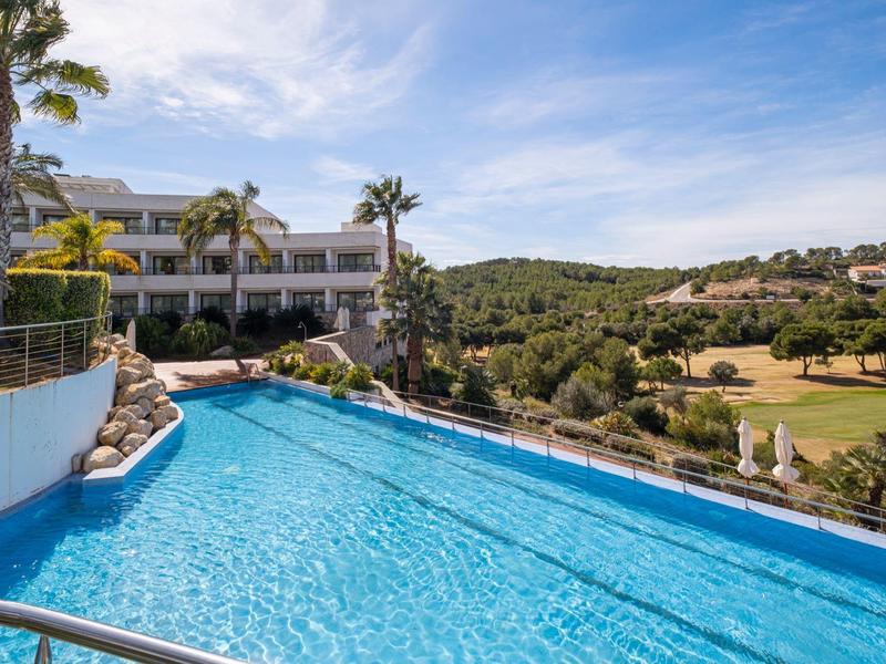 Piscine à débordement avec vue sur des collines verdoyantes et un bâtiment d'hôtel sous un ciel bleu.