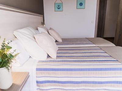 Bright hotel room with neatly made bed, striped bedding, and pillows.
