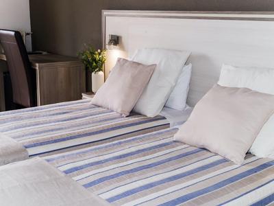 Cozy hotel room with twin beds, striped linens, and soft pillows near a desk and chair.