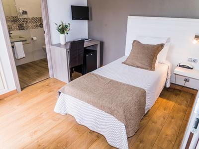 Cozy single hotel room with wooden floor, desk, TV, and bathroom entry.