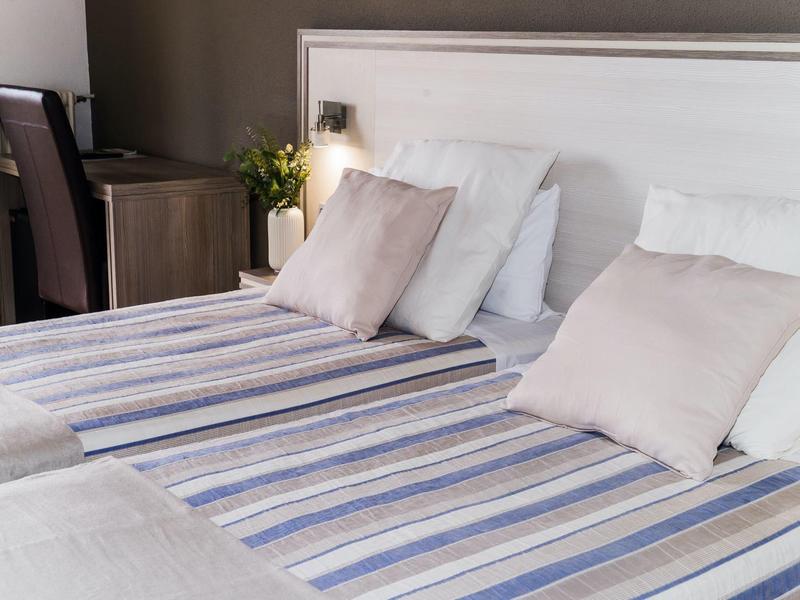 Cozy hotel room with twin beds, striped linens, and soft pillows near a desk and chair.