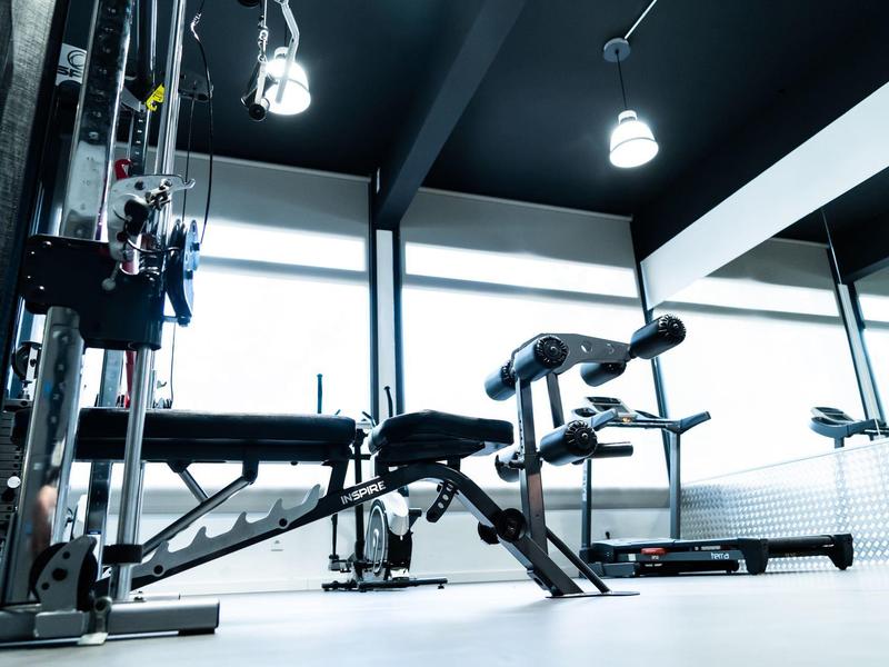 Modern gym with weight machine and benches under large windows.