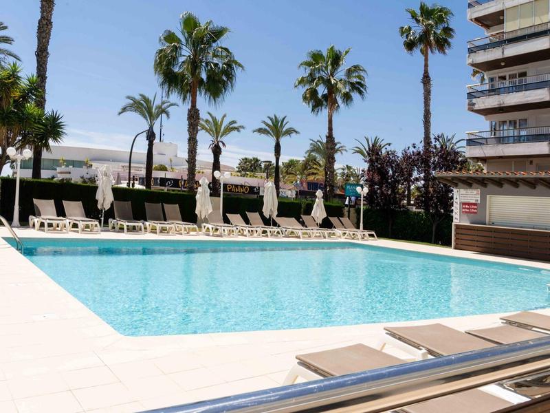 Modern pool area with lounge chairs and palm trees beside a hotel building.