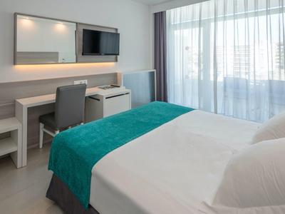 Habitación de hotel moderna con cama doble, escritorio, TV y ventana grande con cortinas.