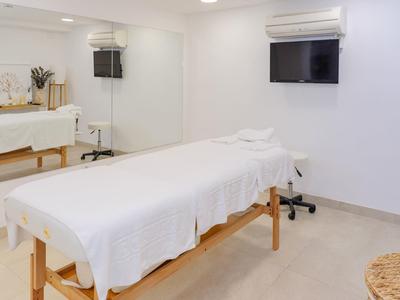 Habitación de masaje con camilla, toallas blancas y televisión en la pared.