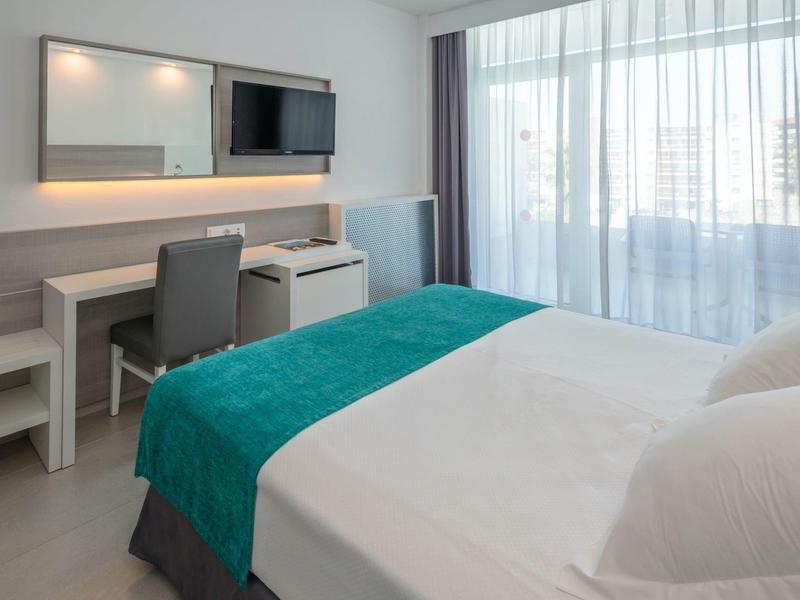 Habitación de hotel moderna con cama doble, escritorio, TV y ventana grande con cortinas.