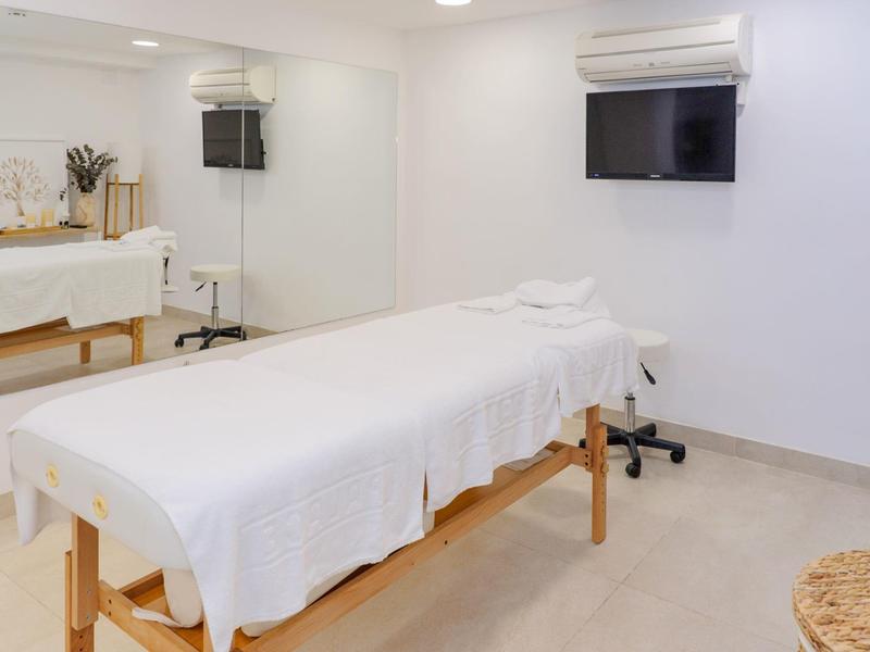Habitación de masaje con camilla, toallas blancas y televisión en la pared.