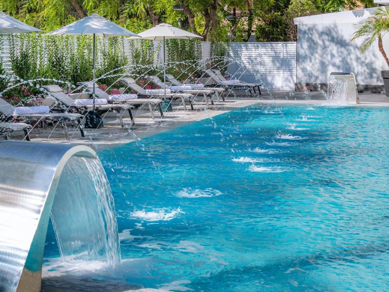 Piscina de hotel moderna con cascada y tumbonas en área exterior soleada.