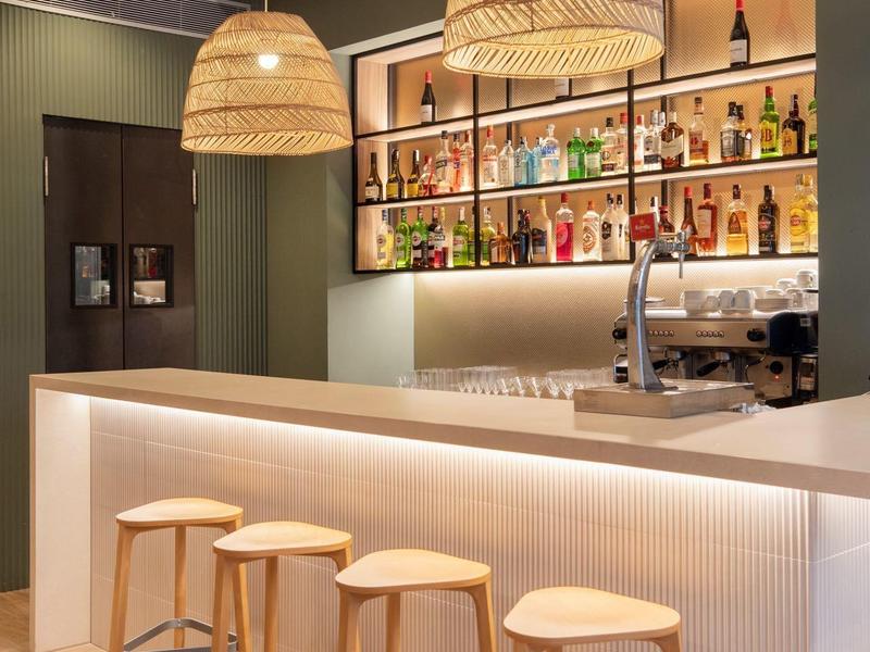 Modern hotel bar area with white counters, four wooden stools, and two woven pendant lights.
