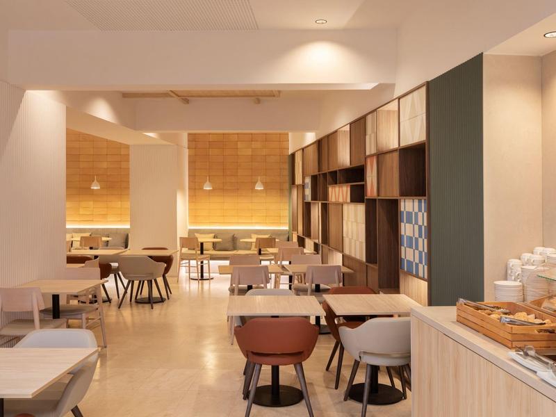 Modern breakfast room with tables, chairs, and buffet in a warmly lit setting.