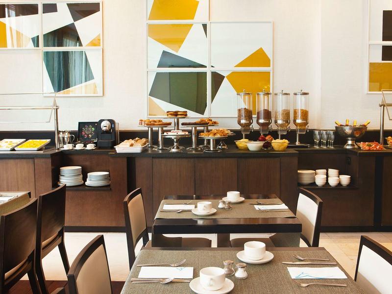 Salle de petit-déjeuner lumineuse avec tables dressées et buffet au design moderne.