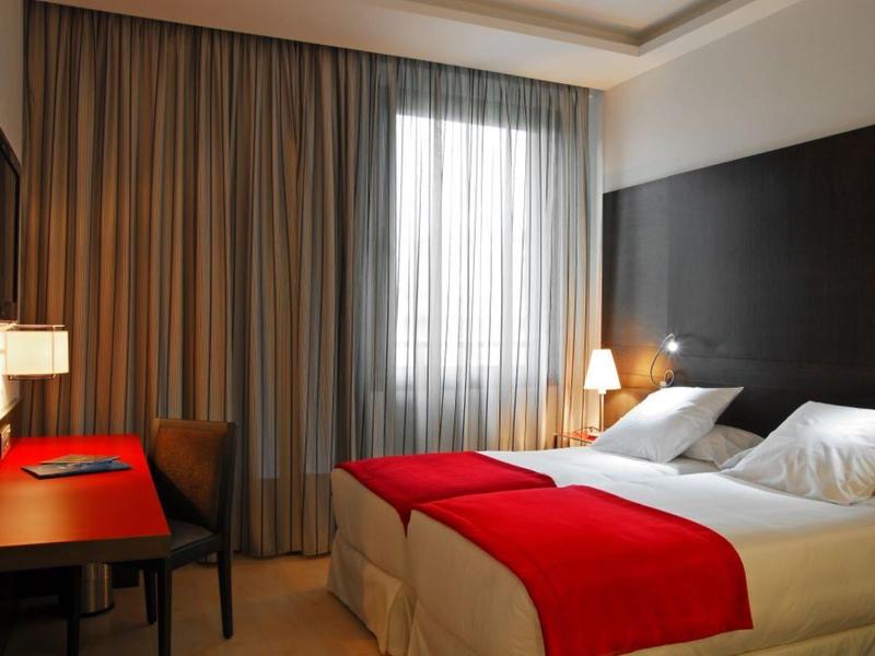 Chambre d'hôtel moderne avec deux lits simples, jetés de lit rouges et bureau près de la fenêtre.