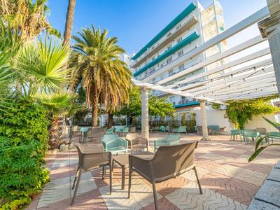 Terrace with seating and view of a multi-story hotel building, surrounded by palm trees.