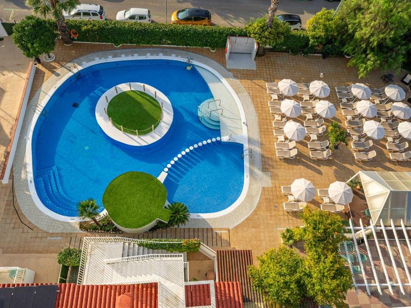 Bird's-eye view of a pool with an island and sun loungers beside white parasols in the hotel garden.