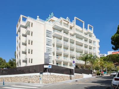 Moderní vícepatrová hotelová budova pod jasnou modrou oblohou se stromy vedle silnice.