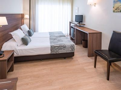 Světý pokoj hotelu se dvěma jednolůžky, psacím stolem, židlemi a dřevěnou podlahou.