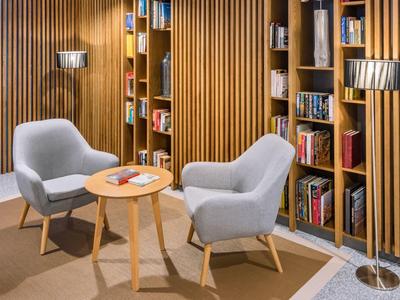 Útulný čtecí koutek se dvěma šedými křesly, malým dřevěným stolkem a knihami na nástěnných policích.