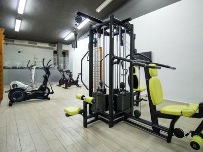 Malá posilovna s fitness stroji a eliptickým trenažérem v hotelovém pokoji.