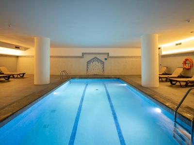 Vytápěný krytý bazén s lehátky a teplým osvětlením v hotelu