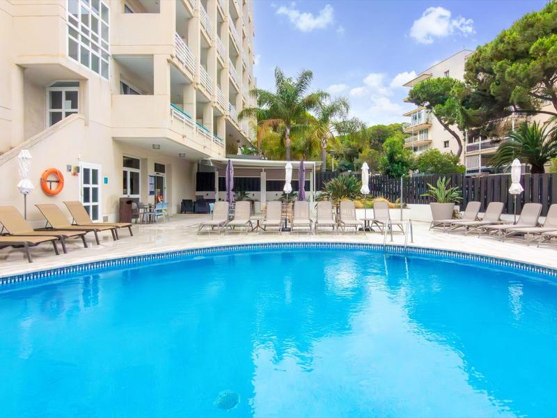 Venkovní hotelový bazén s lehátky a zelenými palmami v pozadí.