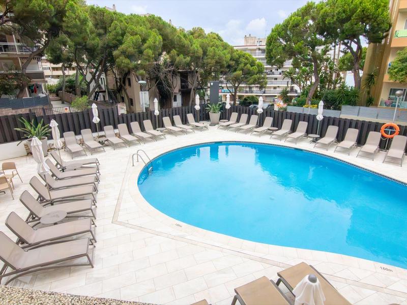 Hotelový bazén s modrou vodou a lehátky v oblasti lemované stromy