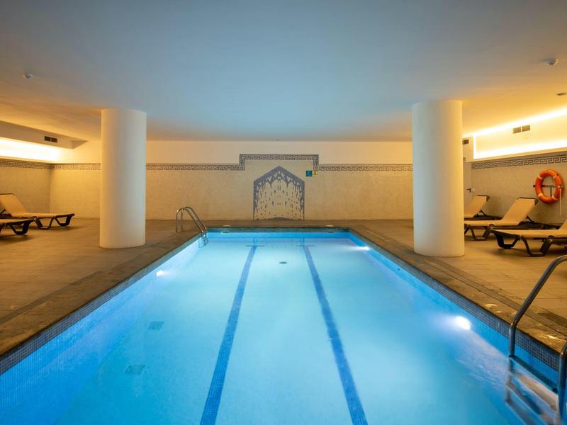 Vytápěný krytý bazén s lehátky a teplým osvětlením v hotelu