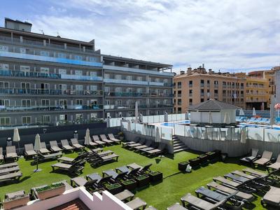 Terrazza soleggiata con sdraio e edifici sullo sfondo sotto un cielo nuvoloso.