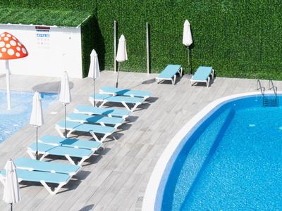 Area piscina con lettini blu, ombrelloni bianchi e piscina con acqua limpida.