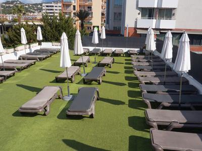 Terrazza sul tetto con lettini e ombrelloni chiusi su prato artificiale verde.
