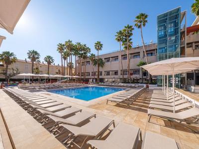 Piscina moderna dell'hotel con lettini e palme sotto un cielo limpido.