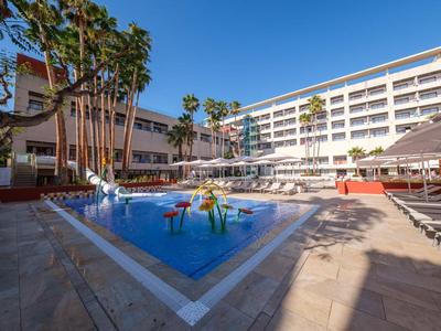 Hotel con grande piscina, palme e lettini in una giornata soleggiata.