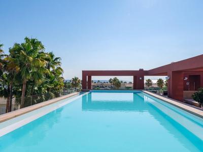 Piscina d'hotel moderna con acqua azzurra limpida, circondata da palme e architettura rossa.