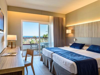 Camera d'hotel moderna con due letti singoli, scrivania e balcone con vista sulla città.