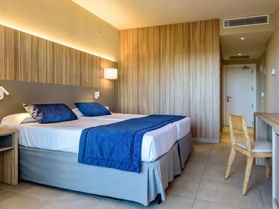 Chambre d'hôtel avec deux lits simples, couvertures bleues, panneaux muraux en bois et bureau avec chaise.