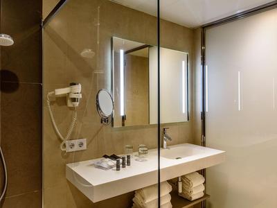 Salle de bain d'hôtel moderne avec grande douche en verre, double lavabo et miroir éclairé.