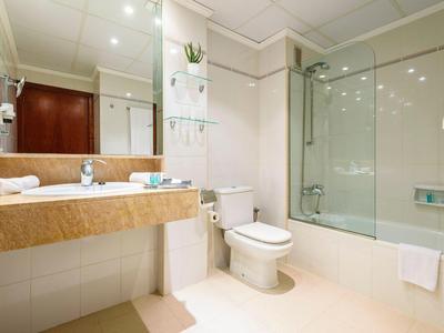 Salle de bains d'hôtel lumineuse avec lavabo, toilette et douche avec paroi en verre.