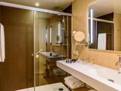 Salle de bain moderne avec grande douche en verre, long plan de travail blanc et miroir éclairé.