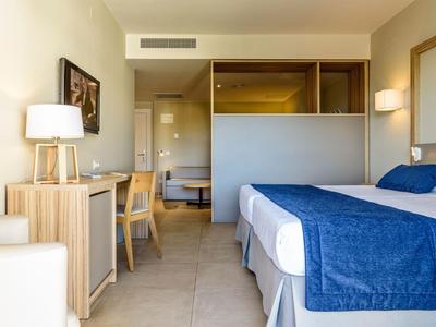 Chambre d'hôtel avec lit double, linge de lit bleu, bureau, chaise et éclairage chaleureux.