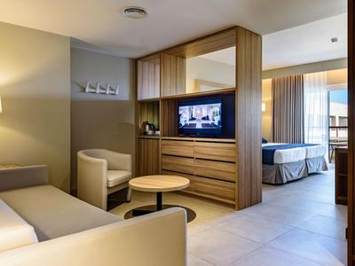 Chambre d'hôtel moderne avec coin salon, télévision et chambre attenante.